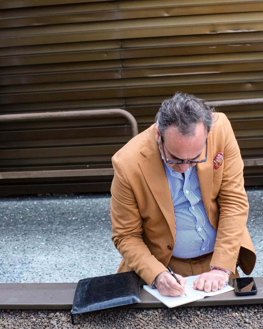 a man in a yellow jacket with a stylish pocket square signs a document