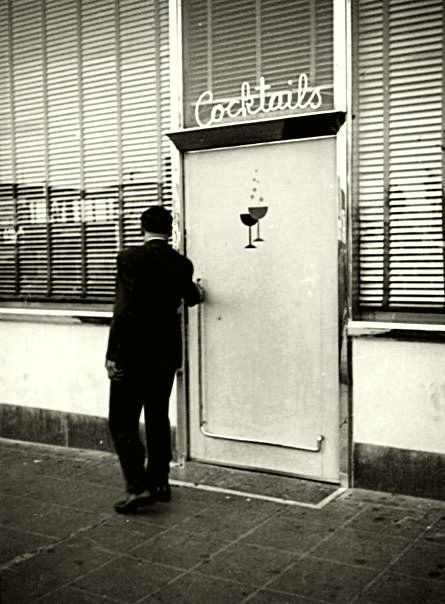 Black and white photograph of a man at the entrance of a vintage cocktail bar, emphasizing the nostalgic charm and history associated with the Old Fashioned cocktail