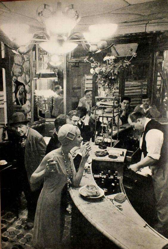 Historic bar interior with a bartender at a polished wooden counter, flanked by traditional paintings, evoking the timeless atmosphere perfect for savoring a Classic Old Fashioned cocktail