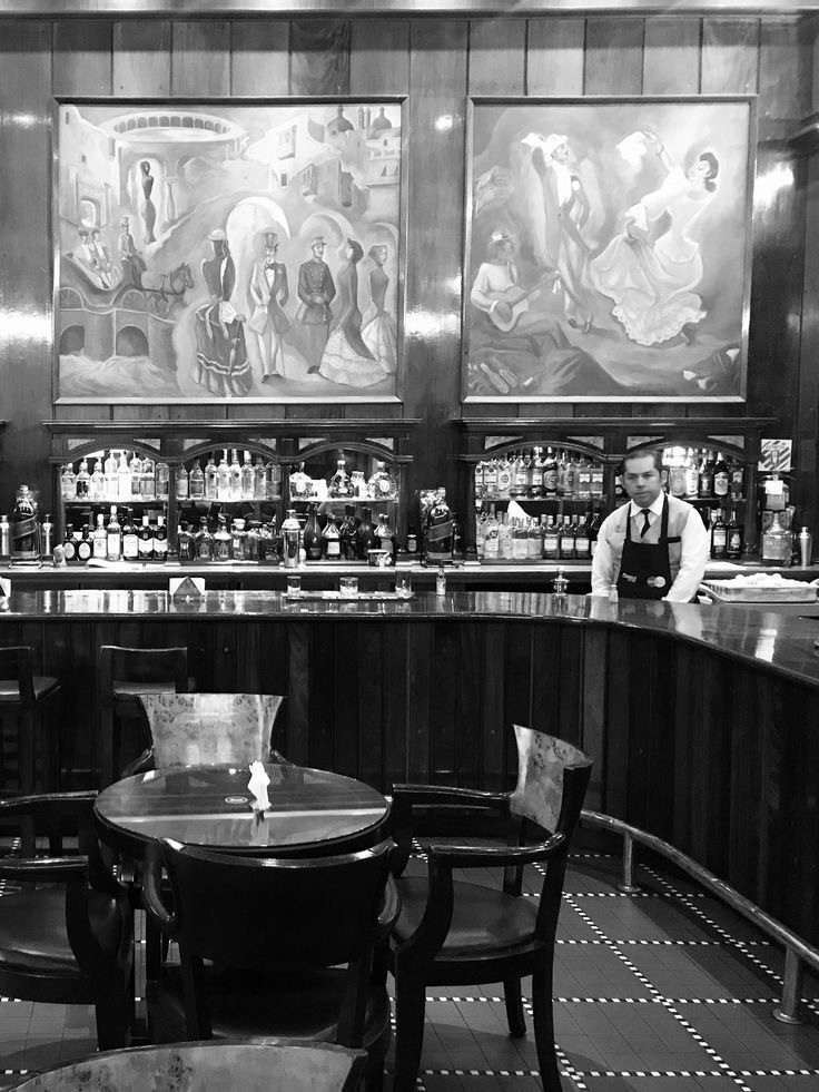 Vintage bar scene with a bartender behind a wooden counter, surrounded by classic artwork, capturing the old-fashioned ambiance ideal for enjoying a traditional Old Fashioned cocktail