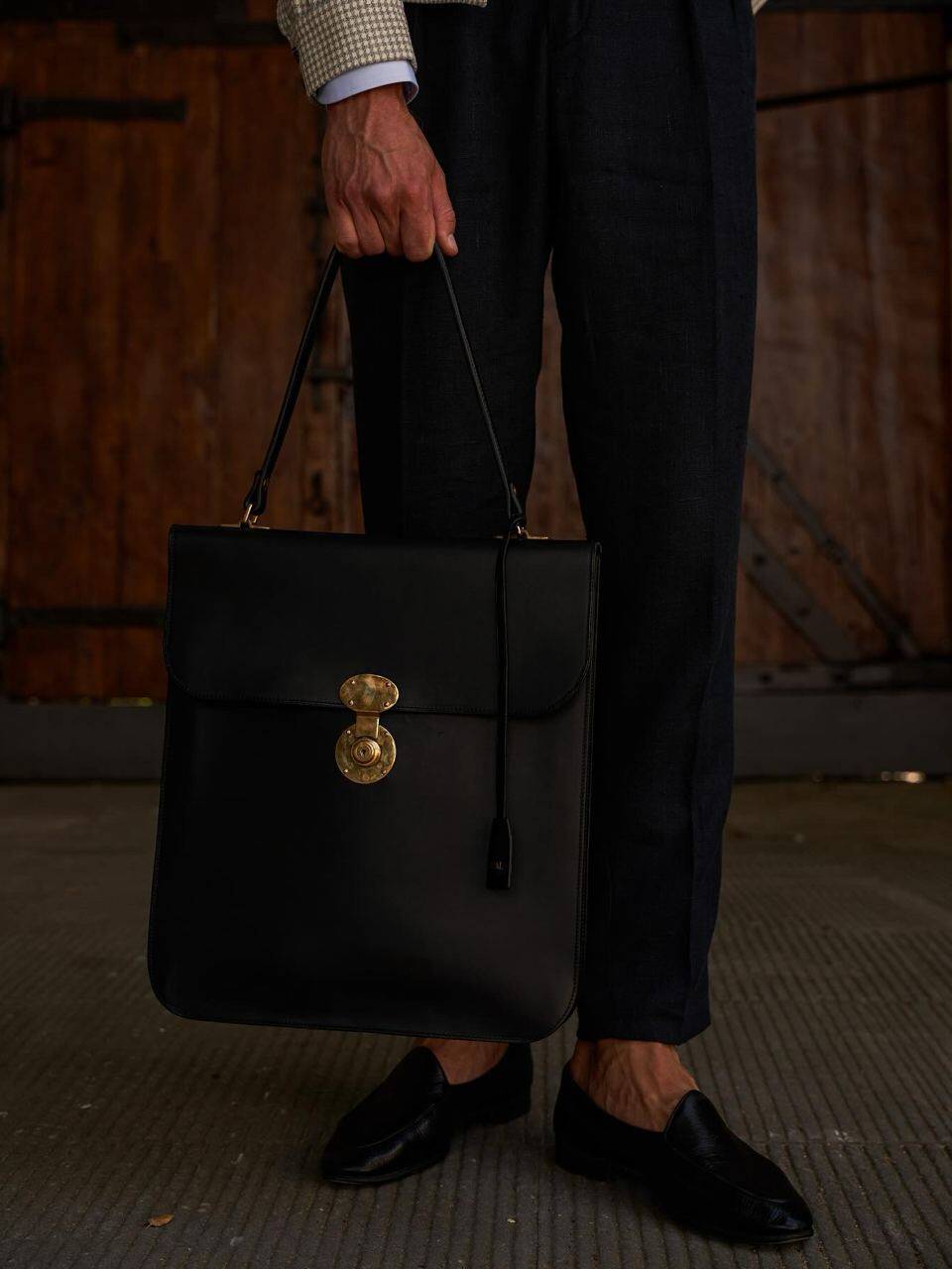 Model in a stylish outfit holding a black leather portfolio, representing high-end fashion and refined accessories