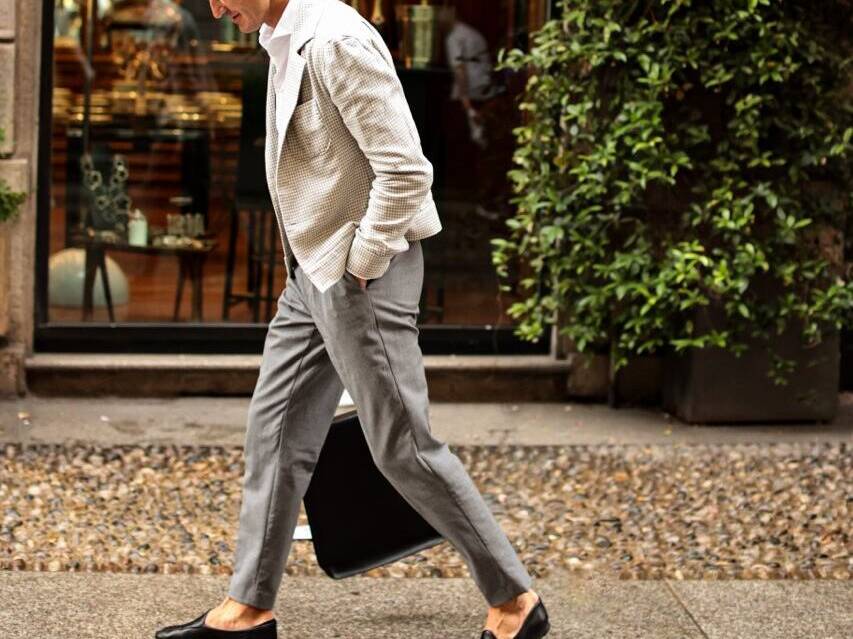 A stylish man in a light plaid blazer, grey trousers, and black loafers showcasing fall trends in a modern city setting. What to wear this fall for a polished, casual look