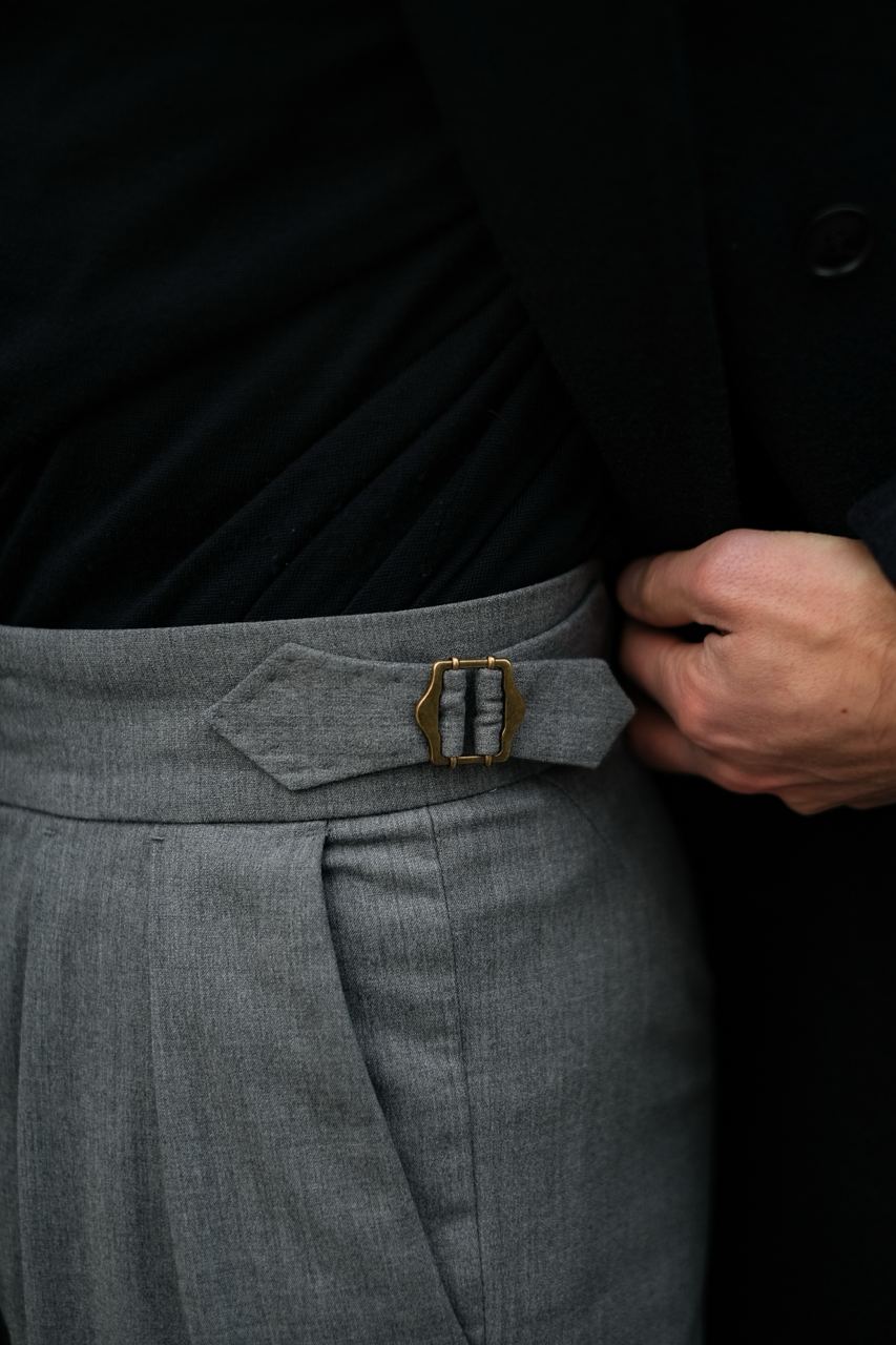 Close-up of grey double-pleated trousers with side adjusters. The trousers showcase sharp pleats, enhancing the structure and fit. This style is perfect for anyone seeking advice on how to choose double-pleated trousers for a sophisticated, modern outfit