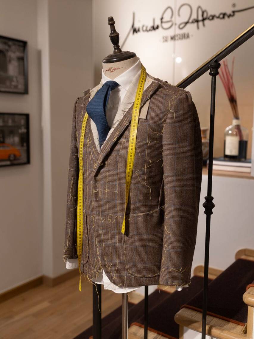 Expert tailor showcasing fabric selections and suit designs at a Milan workshop, emphasizing Italian craftsmanship and bespoke men's fashion