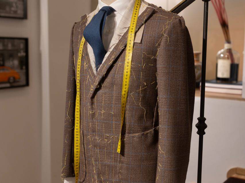 Expert tailor showcasing fabric selections and suit designs at a Milan workshop, emphasizing Italian craftsmanship and bespoke men's fashion