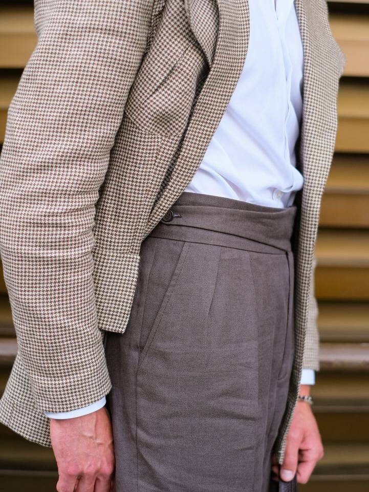 Man wearing brown double-pleated trousers and a checkered blazer. How to choose double-pleated trousers for formal outfits.